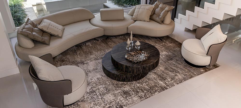 Modern living room with a curved beige sofa, round coffee tables, matching armchairs, and decorative pillows on a textured area rug.