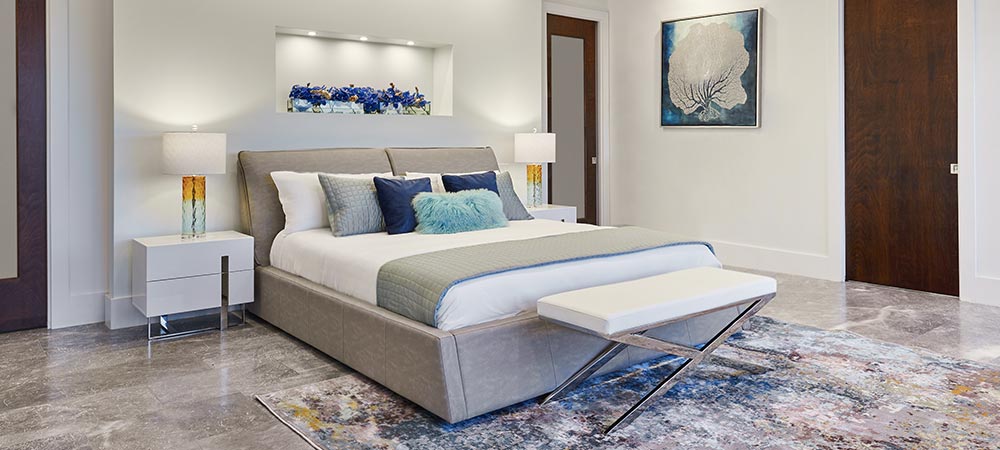 Luxurious bedroom with a modern upholstered bed, white and blue pillows, elegant nightstands, a built-in shelf with blue flowers, and a stylish bench.