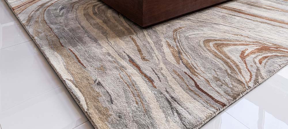 Neutral-toned contemporary rug with a swirl pattern styled beneath a modern wooden coffee table in a living room with glossy tile floors.