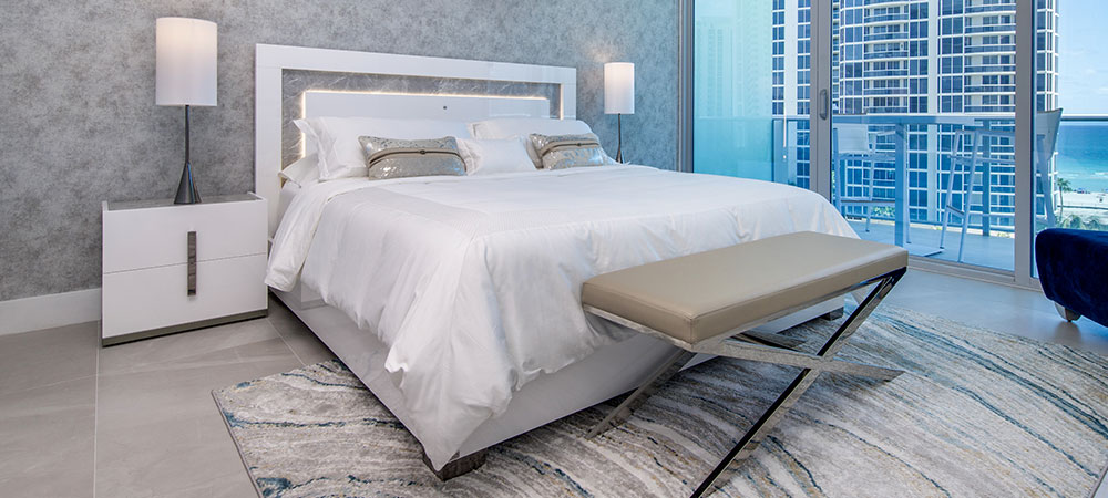 Modern apartment bedroom with city view and a white lacquer bed that feature LED lighting on the headboard and stunning white lacquer nightstnd witha stainless steel accent that doubles as a handle