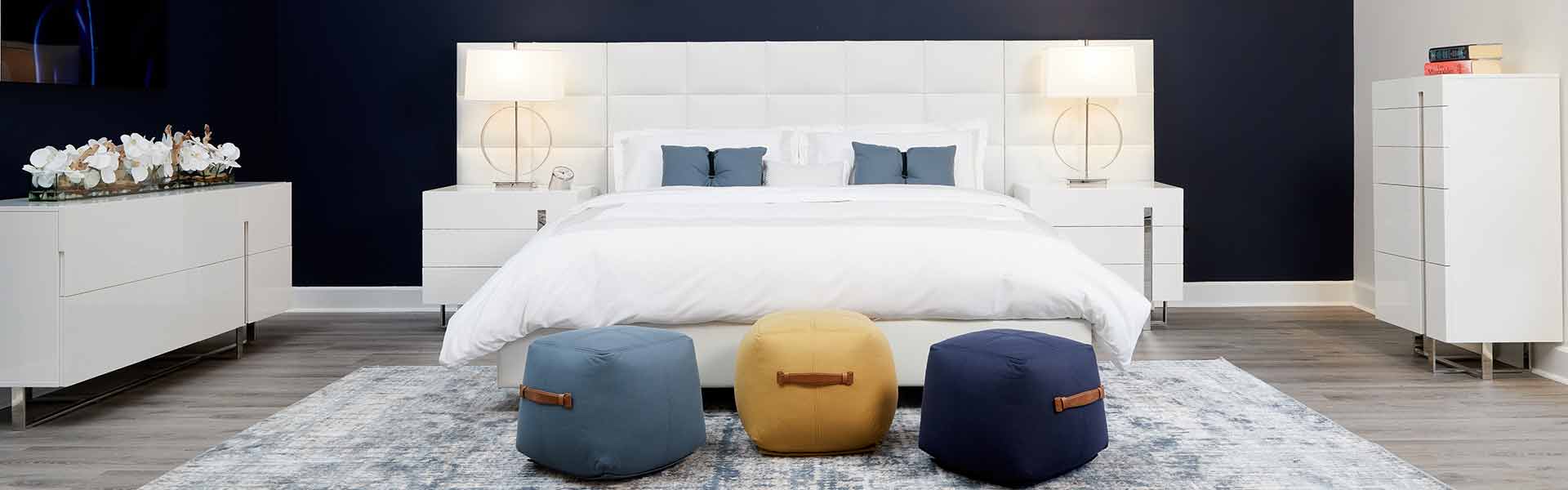  Modern bedroom design with a stylish white Queen bed with leather side panels and minimalist nightstands, sleek table lamps, highlighted against a bold navy blue wall.