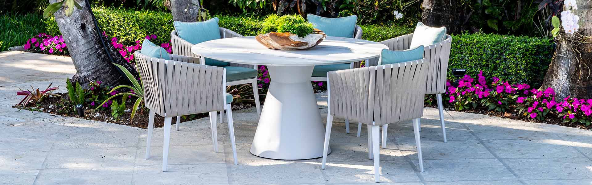 Outdoor modern dining setup with a chic white marble top patio table and contemporary ribbed chairs, surrounded by lush greenery and vibrant pink blooms.