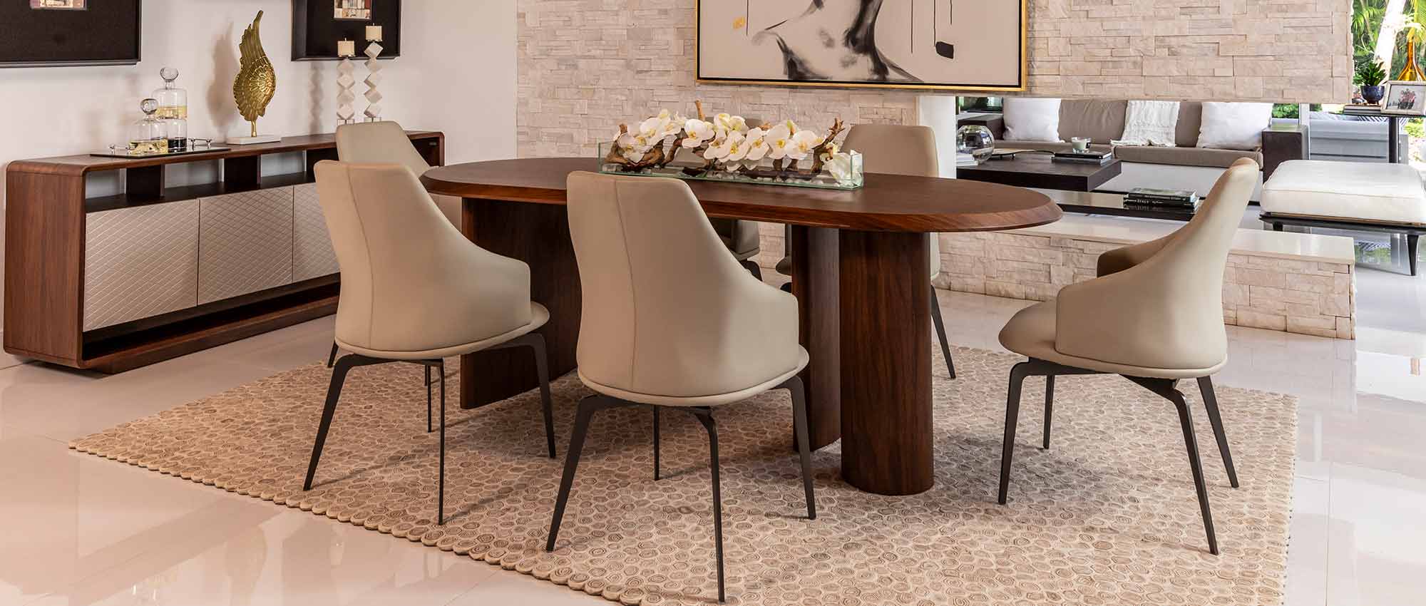 A modern dining room with a white lacquer dining table, grey chairs, and a blue orchid floral table centerpiece. There is a large window that lets in natural light.