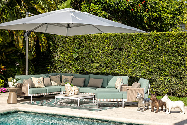 Outdoor patio with green sofa, white umbrella, and garden backdrop by a pool.